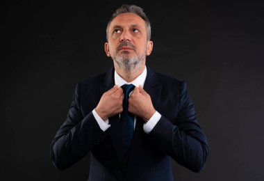 Takım elbiseli orta yaşlı bir adam, yukarı bakarken kravatını düzeltiyor, hırsı, umudu, vizyonu veya kurumsal bir ortamda yansımayı simgeliyor..