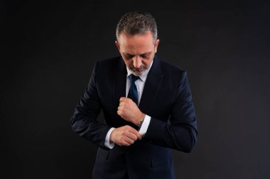 Takım elbiseli olgun bir adam gömleğinin kolunu ve saatini düzeltiyor, resmi bir olaya ya da iş toplantısına hazırlanıyor..