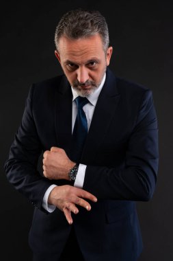 Donanma takımı giymiş olgun bir işadamı gömleğinin kolunu düzeltiyor ve kameraya ciddi ciddi bakıyor. Güven, zarafet ve profesyonellik kavramı.