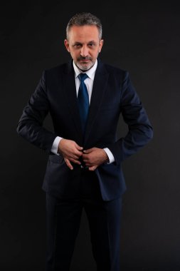 Olgun iş adamı resmi kıyafetini ayarlıyor, donanma ceketinin düğmelerini iliklerken kameraya güvenle bakıyor..