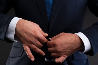 Koyu renk ceketinin düğmelerini ilikleyen bir adamın ellerine yakın çekim, profesyonel giysiler içinde zarafet ve dikkat gösterilir..