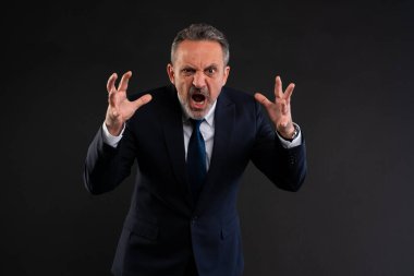 Resmi takım elbiseli öfkeli iş adamı elleri havada bağırıyor, hayal kırıklığı, öfke ya da stres gösteriyor. Stüdyo çekimi koyu arkaplanda