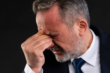 Takım elbiseli olgun bir iş adamının yakın çekimi. Alnını tutarken acı çekiyor. Baş ağrısını, stresi ya da rahatsızlığı simgeliyor..