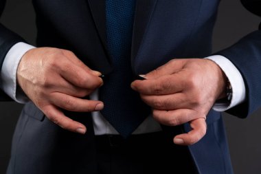Bir iş adamının elleri, lacivert takımının düğmelerini iliklerken zarafet ve profesyonel stili vurguluyor.