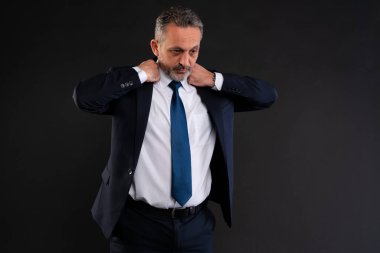 İş elbisesi giymiş olgun bir adam takım elbisesinin yakasını düzeltiyor, resmi bir etkinliğe ya da toplantıya hazırlanıyor..