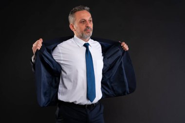 Tişört ve kravat giymiş, koyu mavi bir ceket giyen, işe ya da işe hazırlanan kendine güvenen olgun bir adam..