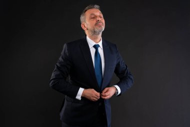Kendine güvenen olgun bir adam donanma ceketinin düğmelerini ilikliyor, soğukkanlılığını ve resmi bir olaya veya iş durumuna hazır olduğunu ifade ediyor..
