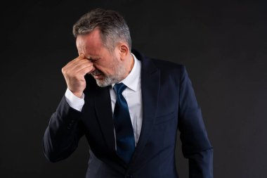 Siyah bir arka planda elini yüzüne bastıran orta yaşlı bir işadamı hayal kırıklığı, stres ya da baş ağrısı belirtileri gösteriyor..