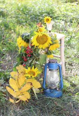 Ayçiçekleri, sarı yapraklar, eski bir fener ve kırsal bir bahçede eski bir sandalye.