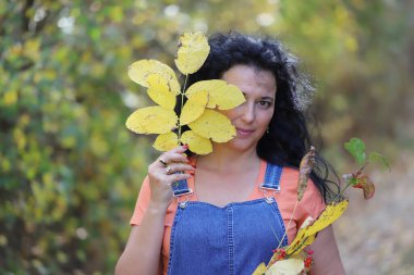 Parlak sonbahar yolunda uzun kıvırcık saçlı, güzel bir esmer. Açık havada çekilmiş.
