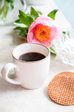 Kahve zamanı konsepti, seramik bir fincan sade kahve, bisküvi ve mermer bir yüzey üzerinde güzel pembe şakayıklar, stüdyo çekimi.