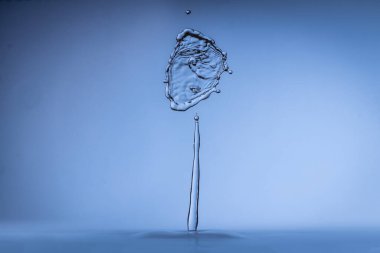 Açık mavi arka planda serin su sıçraması. Soyut, ilginç, yaratıcı. Çarpıştıkları zaman iki su damlasının güzel yaratılışı.