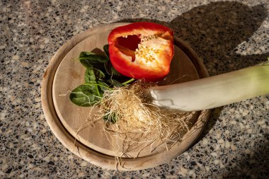 Tahta tabak, yarısı kesilmiş kırmızı biber, yeşil ıspanak yaprakları ve kıllı pırasa. Salata, yemek ve atıştırmalık hazırlarken mutfaktan görüntü. Sebze dengeli beslenme için sağlıklı bir seçenektir..