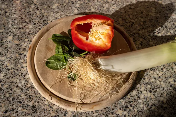 Tahta tabak, yarısı kesilmiş kırmızı biber, yeşil ıspanak yaprakları ve kıllı pırasa. Salata, yemek ve atıştırmalık hazırlarken mutfaktan görüntü. Sebze dengeli beslenme için sağlıklı bir seçenektir..