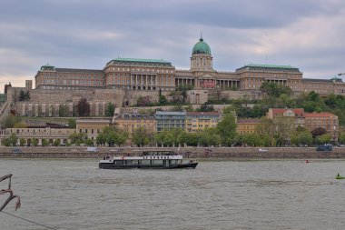 Budapeşte, Macaristan - 28 Nisan 2023: Nehirden Kraliyet Sarayı ve ulusal galeriye manzara. Tuna 'da eğlence teknesi yüzüyor. Turistler eski şehri geziyor..