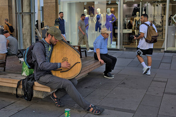 Вена, Австрия - 29 июня 2023 года: Неизвестный музыкант играет на выщипанном музыкальном инструменте. Вид на одну из типичных улиц исторического центра Вены. Улицы и архитектура старого города.