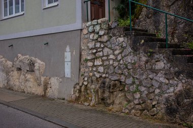 Dağ yamacında merdivenleri olan eski taş duvar. Taşların arasında büyüyen bitki örtüsü ona eski bir görünüm kazandırıyor. Evin temeline kısmen entegre olmuş bir duvar. Hallstatt, Avusturya.