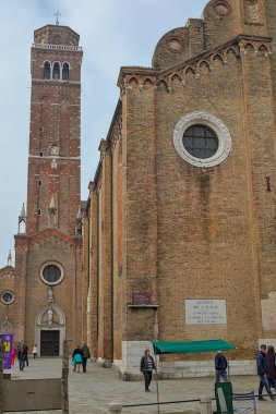 Venice, Italy - October 15, 2024: People near the majestic Basilica of Santa Maria Gloriosa dei Frari (the Frari) in Venice. The bell tower, built of rough red brick, shows classical Gothic elements. clipart