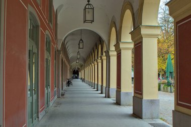 Münih 'te uzun süre kapalı kalan oyun salonu, zarif bir ortam yayarak mesafeye kadar uzanıyor. Hofgarten 'in yüksek kemer ve sütunlarının ritmik tekrarı büyüleyici bir perspektif yaratır..