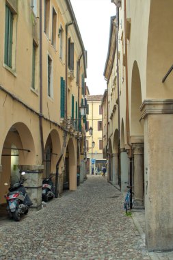 Padova, İtalya - 17 Ekim 2024: Padua, İtalya 'da dar bir kaldırım taşı caddesi eski binalar arasında esiyor. Scooter 'lar kemerli duvarların altında sessizce dinlenir. Yıpranmış taş kolonların yanında bir bisiklet duruyor..