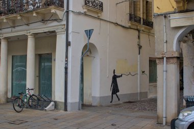 Padova, İtalya - 17 Ekim 2024: Bir siluet adam boyalı bir kedinin yanında yürüyor. Yumuşak bir köşe duvarı boyunca uzanıyorlar. Sakin renkler sessiz sokak cazibesiyle buluşur.