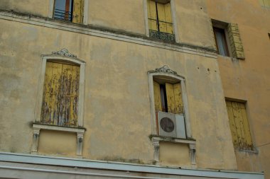 Sarı panjurlar çatlamış ve yağmur ve güneş yüzünden soyulmuş. Yalnız bir klima kemerli pencerelerden birinin altında duruyor. Eski bina eski zamanların hikayelerini fısıldıyor..