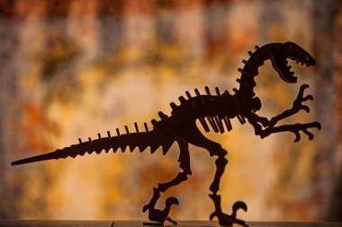 Bir Velociraptor siluetinin ahşap modeli. Renkli bulanık bir arka plana karşı.