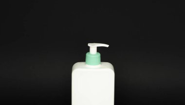 Sıvı sabun, şampuan ve siyah arka planda jöle içeren beyaz bir şişe.