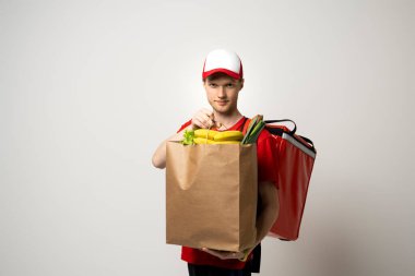 Teslimat konsepti. Yakışıklı teslimatçı marketten bir paket market, meyve, sebze, yiyecek ve içecek taşıyor.