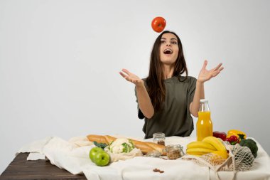 Yeşil tişörtlü mutlu bir kadın sağlıklı sebzeler, meyveler, ekmekler ve evdeki mutfakta atıştırmalıklarla dolu bir alışveriş çantası açıyor. Sağlıklı beslenme vejetaryen konsepti