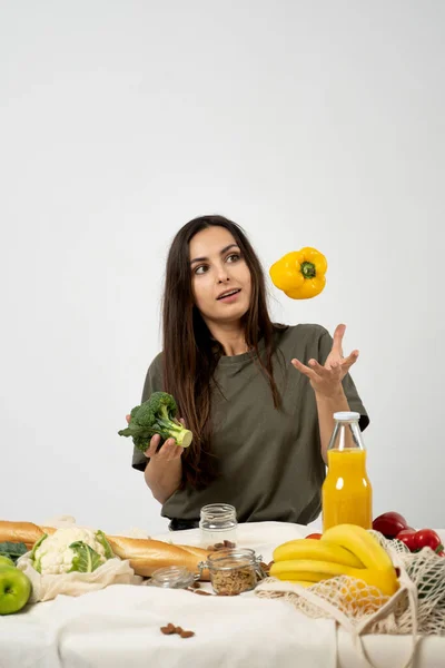 Stock image Happy woman in green t-shirt unpacking shopping mesh eco bag with healthy vegetables, fruits, bread, snacks on the kitchen at home. Healthy eating vegetarian concept