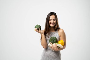 Gülümseyen esmer kız elinde brokoli ve sebzeli örgü alışveriş çantası tutuyor. Plastik poşetsiz yeşillikler. Sıfır atık, plastiksiz çevre dostu kavram. Sürdürülebilir yaşam tarzı