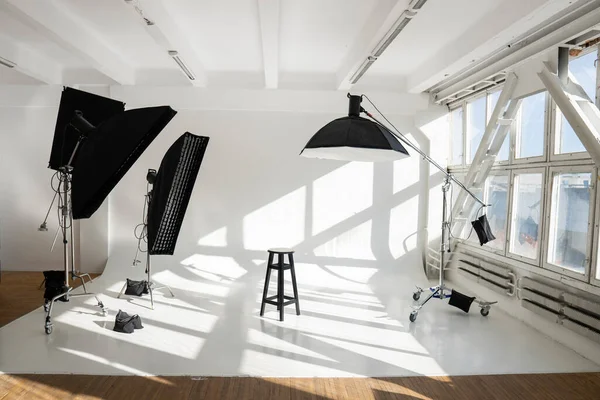 stock image Professional lighting equipment, flashes, c-stands on a cyclorama in modern photo studio with a huge windows. Octabox, stripbox, softbox, buety plate and other stuff for photography