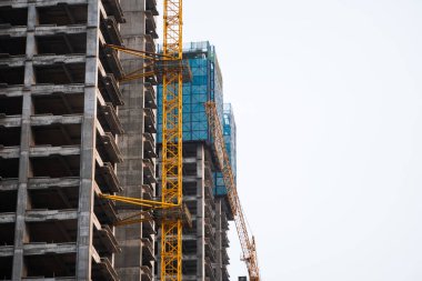 Sarı kule inşaat vinci, bitmemiş çok katlı bir apartmanın üzerinde, açık mavi bir gökyüzüne karşı yükseliyor. Modern monolitik yapı