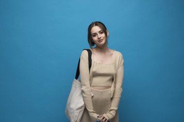 Beyaz stüdyo arka planında duran esmer, neşeli, bin yıllık beyaz bir kadın. Flax marka alışveriş çantası tutan bir kadın. Moda ve ekoloji kavramı