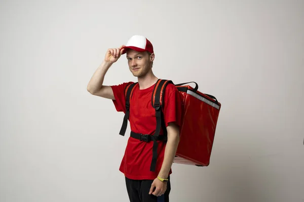 Young delivery guy employee man in red uniform work as courier and hold a red thermal food bag backpack isolated on white background studio. Food delivery dervice concept