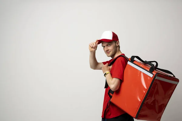 Food Delivery. Side view courier man employee man in red uniform work as courier and hold a red thermal food bag backpack isolated on white background studio