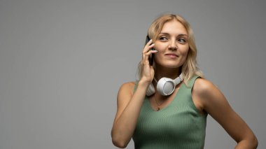 Gülümseyen, yeşil tişörtlü, beyaz kulaklıklı, cep telefonuyla konuşurken yüzünü çeviren mutlu sarışın kadın portresi.