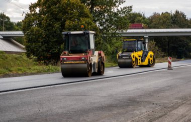 İki ağır asfalt yol silindiri ve ağır titreşimli paten sıkıştırıcısı yol inşaatındaki yolda yeni asfalta baskı yapıyor.