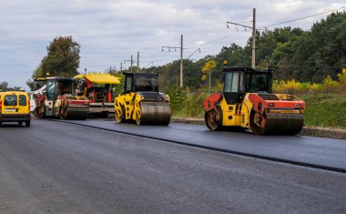 Ağır asfalt yol silindirli, ağır titreşimli paten sıkıştırıcı ve asfalt kaldırımlı yeni asfalt kaldırımlar bir yol inşaatı alanındaki yolda yeni asfalt döşüyorlar.