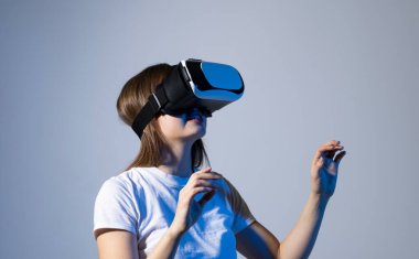 Beyaz tişörtlü esmer kadın VR gözlük takıyor stüdyo arka planına dokunuyor.