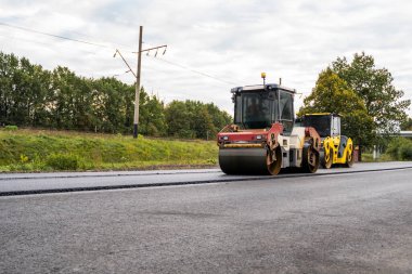 İki ağır asfalt yol silindirli ağır titreşimli paten sıkıştırıcısı yol inşaatındaki yolda yeni asfalta baskı yapıyor.