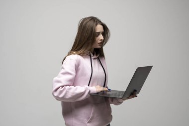Laptop kullanan, pembe kapüşonlu, uzun saçlı konsantre genç bir kadın. Stüdyo görüntüsü, çevrimiçi çalışma kavramı, e-öğrenme veya dijital görevler.