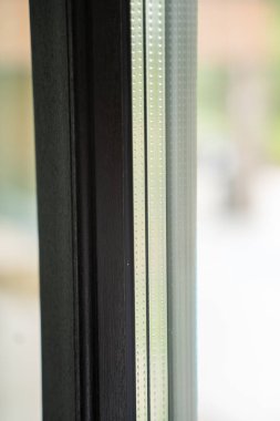 Cam ötesinde çözünmüş orman manzaralı, cam kaplı bir pencerede alüminyum profil ve uzay şeridi üzerine odaklanmış bir çekim..