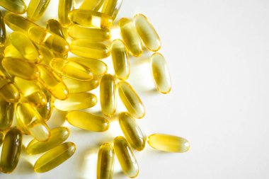 Beyaz bir yüzeye yerleştirilmiş balık yağından yapılmış parlak sarı yumuşak kapsüller. Haplar ışığı yansıtıyor, parlak, şeffaf dokularını ve parlak altın rengini vurguluyor..