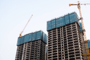 Yapım aşamasındaki iki yüksek açılı beton binanın yüksek açılı fotoğrafı, vinçler ve iskelelerle çevrili, kentsel gelişimi gösteriyor..