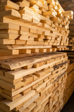 Büyük bir çam yığını atölyenin içinde hava kurutmak için istiflenmiş, güçlü güneş ışığıyla aydınlatılıyor. Tahta tahıl, doku ve doğal kenarlar açıkça görülüyor..