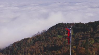 Sonbahar renkli ağaç gölgelerinin ve sisli bir vadinin üzerindeki bayrağın üzerinde yırtık bir Slovenya bayrağını dalgalandırmak. Sonbahar, mevsimler, doğa ve çevre kavramları. 4K, 60FPS