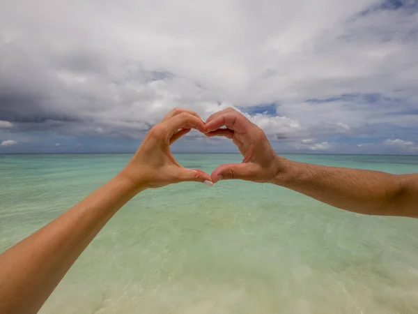 Couple forming a heart with their hands in front of the green Caribbean sea and the blue sky
