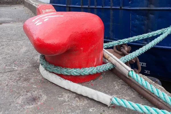 Close-up of a mooring rope with a knotted end tied around a cleat on a wooden pier/ Nautical mooring rope